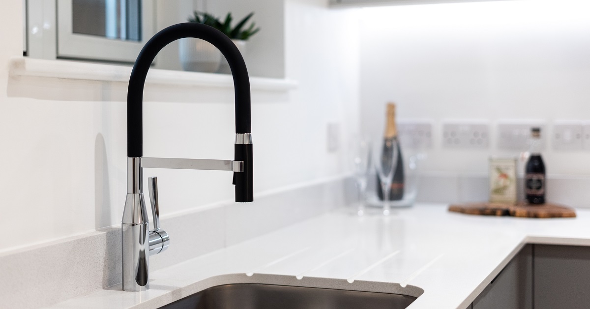 elegant modern kitchen tap which is partly stainless steel and partly black in design with white quartz worktop and under mounted sink with a blurry background